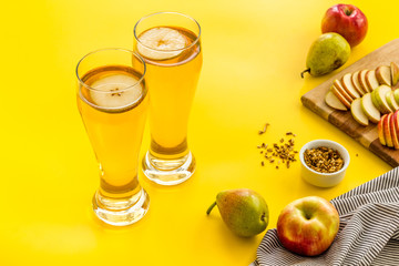 Glasses of beer with apple and peer on yellow desk
