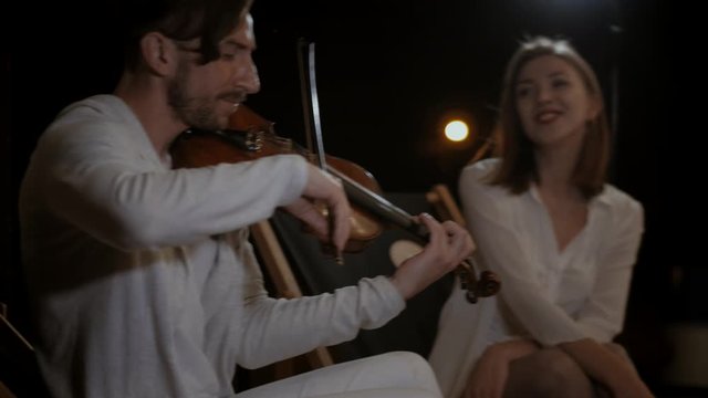 A duo of musicians plays under the night sky. Violinist and girl vocalist playing at a concert on the street at night. Musicians play on the stage of the restaurant.