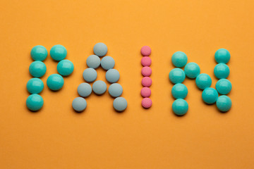 Word pain on orange background written with colorful pills. Painkiller tablets taken by prescription.