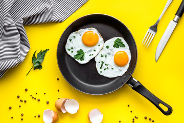 Fried eggs on frying pan on yellow desk top-down
