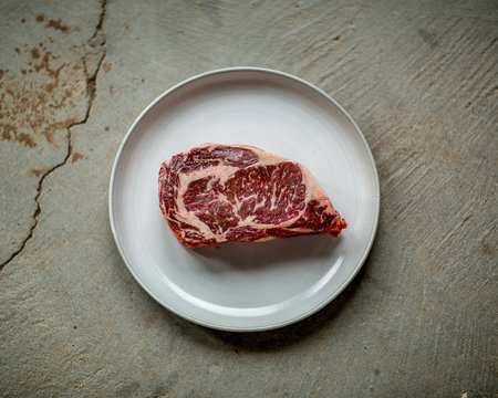 Perfectly Marbled Raw Filet of Steak on a Plate and Grunge Concrete Table