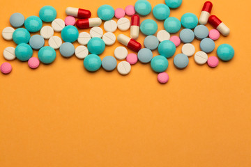Obraz premium Lot of multicolored pills and tablets on orange background with free space for text or prescription.