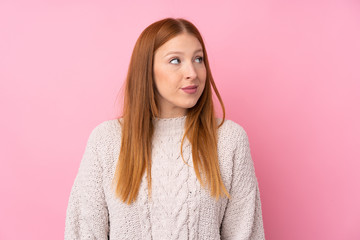 Young redhead woman over isolated pink background making doubts gesture looking side