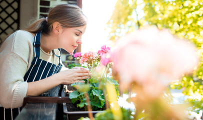 Beautiful woman smelling flowers on balcony, take care of plants at home