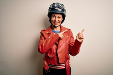 Middle age motorcyclist woman wearing motorcycle helmet and jacket over white background smiling and looking at the camera pointing with two hands and fingers to the side.