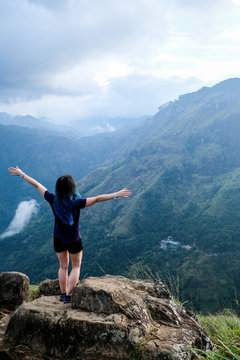 A young girl with a long blue hair staying on the edge of a cliff. Famous hill in southern Sri Lanka known as Little Adam's Peak. Feeling freedom and staying healthy in isolation hiking in Asia.