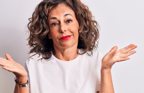 Middle age beautiful brunette woman wearing casual t-shirt standing over white background clueless and confused with open arms, no idea and doubtful face.