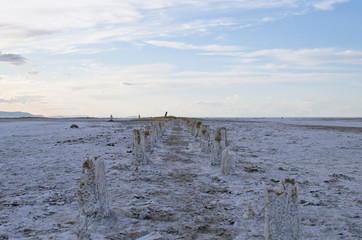Fototapeta na wymiar The long view of the old and broken pier post along the salty salt flat floors in the lakebed. 
