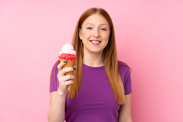 Young redhead woman with a cornet ice cream over isolated pink background smiling a lot