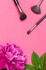 Obraz na płótnie Canvas Professional Different makeup brushes with pink spring peonies flowers on pink background flat lay top view copy space. Beauty product, makeup, women's accessory, fashion. Cosmetic makeup Set