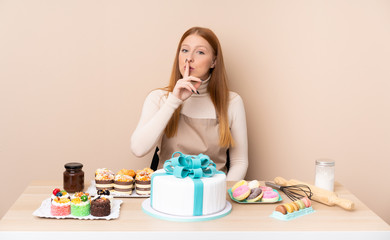 Obraz na płótnie Canvas Young redhead woman with a big cake doing silence gesture