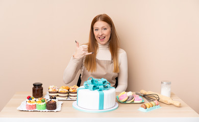 Obraz na płótnie Canvas Young redhead woman with a big cake making phone gesture