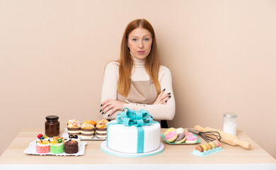 Obraz na płótnie Canvas Young redhead woman with a big cake keeping arms crossed