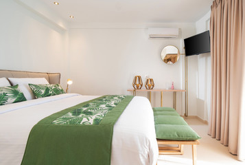 Modern ecological style interior of hotel room with empty wall copy space. Side view of white bedroom with green palm leaves bedding