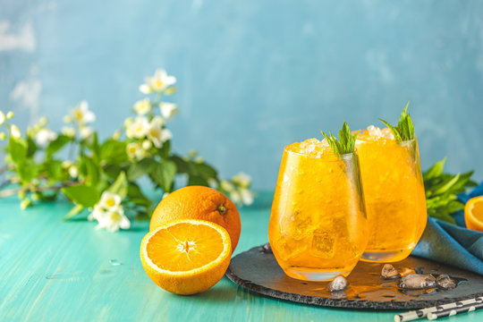Two glass of orange ice drink with fresh mint on wooden turquoise table surface. Alcoholic non-alcoholic drink-beverage.