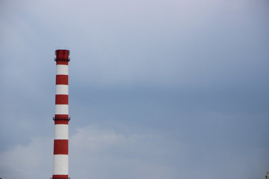 Red and white factory chimney, on cloudy sky. Polution concept