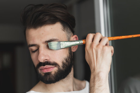 portrait of a bearded man holding artistic tools and preparing to paint a picture