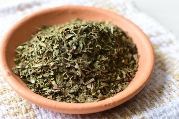 Fototapeta premium Chopped dried leaves of basil leaves on white wooden background