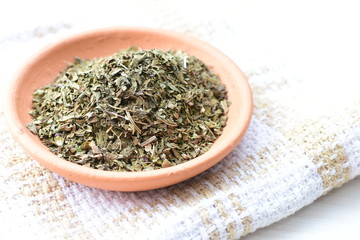 Chopped dried leaves of basil leaves on white wooden background