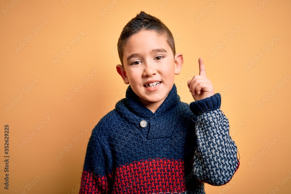 Canvas Prints Young little boy kid wearing winter sweater over yellow isolated background pointing finger up with successful idea. Exited and happy. Number one.