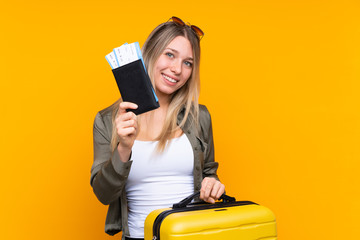 Young blonde woman over isolated yellow background in vacation with suitcase and passport