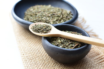 Chopped dried leaves of basil leaves on white wooden background
