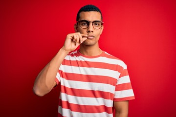 Young handsome african american man wearing casual striped t-shirt and glasses mouth and lips shut...