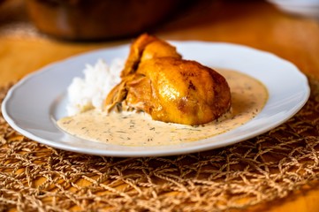 Roasted chicken leg with dill sauce and stewed rice on plate on table.