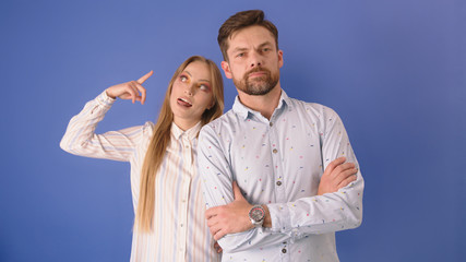 Young couple isolated on the blue background. Woman gesticulation showing the boyfriend, husband is crazy.