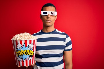 Young handsome african american man watching movie using 3d glasses eating popcorns Relaxed with serious expression on face. Simple and natural looking at the camera.