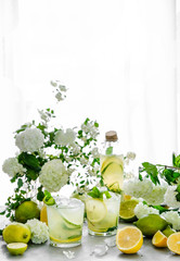Summer composition. The table is strewn with garden flowers. Hydrangeas, jasmine, daisies in the morning sun. Fresh citrus lemonade is poured into glasses. Ice is scattered on the table. it melts, cre