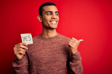 Young handsome african american man holding reminder paper with yes message pointing and showing...