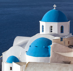 Blue-domed Greek church and belfry against volcano caldera in Oia town on Santorini island,...