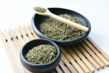 Chopped dried leaves of basil leaves on white wooden background