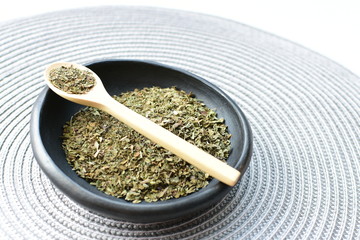 Chopped dried leaves of basil leaves on white wooden background