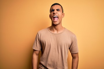 Young handsome african american man wearing casual t-shirt standing over yellow background angry...