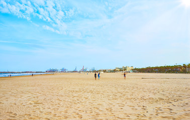 People walking on the sand of a large beach.