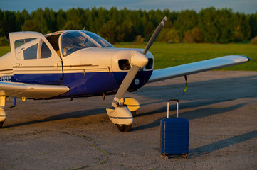 A blue suitcase and a landed small private jet. Four-seater plane with a propeller for the air...