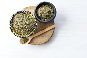 Chopped dried leaves of basil leaves on white wooden background