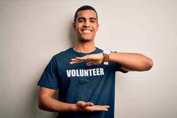 Young handsome african american man volunteering wearing t-shirt with volunteer message gesturing with hands showing big and large size sign, measure symbol. Smiling looking at the camera. Measuring