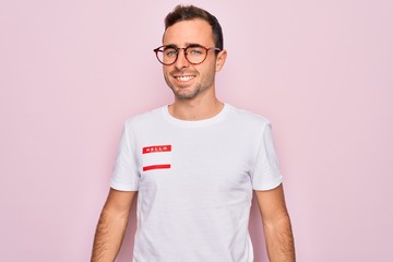 Handsome man with blue eyes wearing sticker with hello my name is message identification with a...