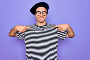 Handsome man with blue eyes wearing striped t-shirt and french beret over purple background looking...