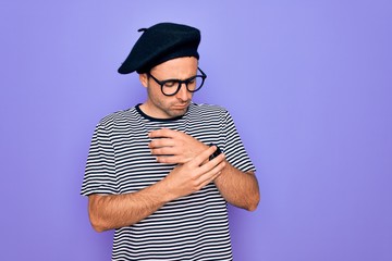 Handsome man with blue eyes wearing striped t-shirt and french beret over purple background...