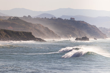 Landscape of a rocky shoreline with waves breaking at sunset in a windy day. Horizontal image