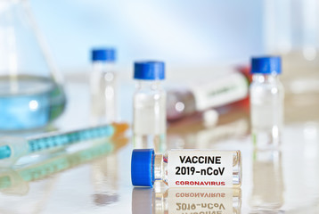 Coronavirus Covid 19 vaccine concept small glass vials with blue caps on white table, green orange syringe near closeup detail