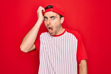 Young handsome sporty man with blue eyes wearing striped baseball t-shirt and cap surprised with...