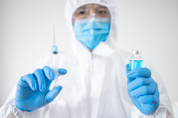 COVID-19 Vaccination concept. Doctor or physician in Personal protective equipment suit (PPE) with mask, goggles and rubber gloves holding syringe and medicine vial for Coronavirus vaccine injection.