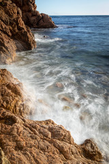 Landscape of a rocky shoreline with waves breaking at sunset. Vertical image