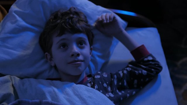 The boy lies in bed and wants to sleep. Dreams in His Bedroom at Night