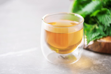 Cup of healthy herbal tea with nettle. Alternative herbal medicine. Stinging nettles, urtica. Skin allergy care. Fresh stinging nettles on grey background.